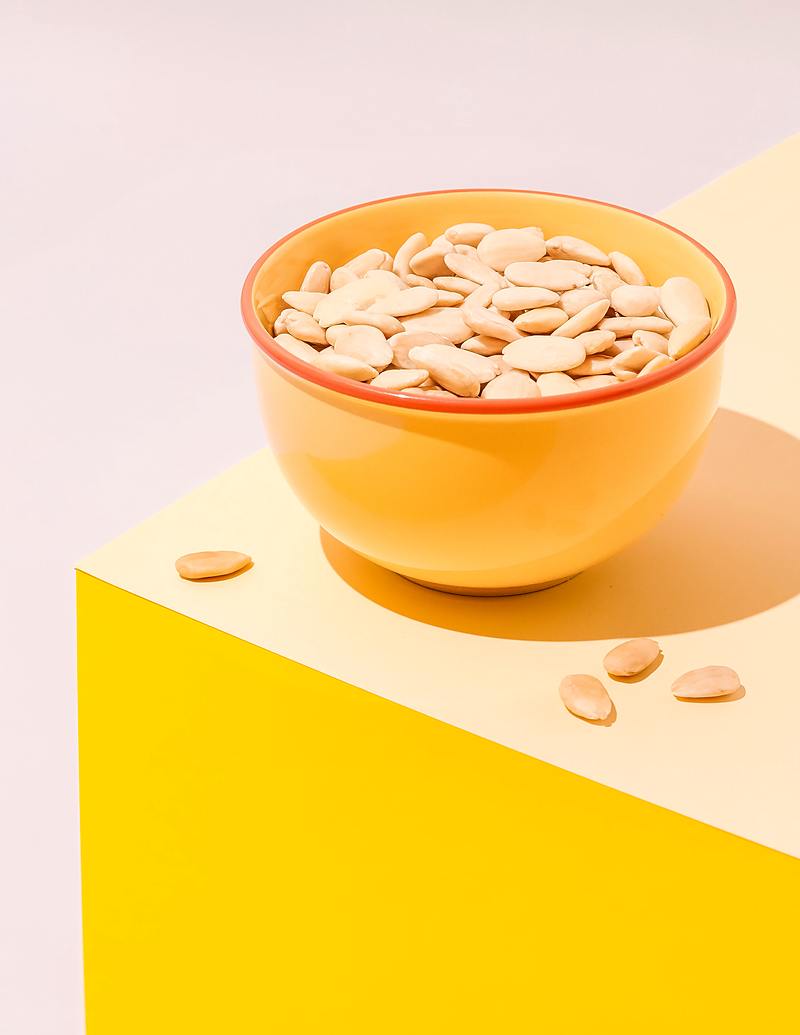 Amandes entières blanchies dans un bol jaune à liseré rouge, sur un plan crème et jaune