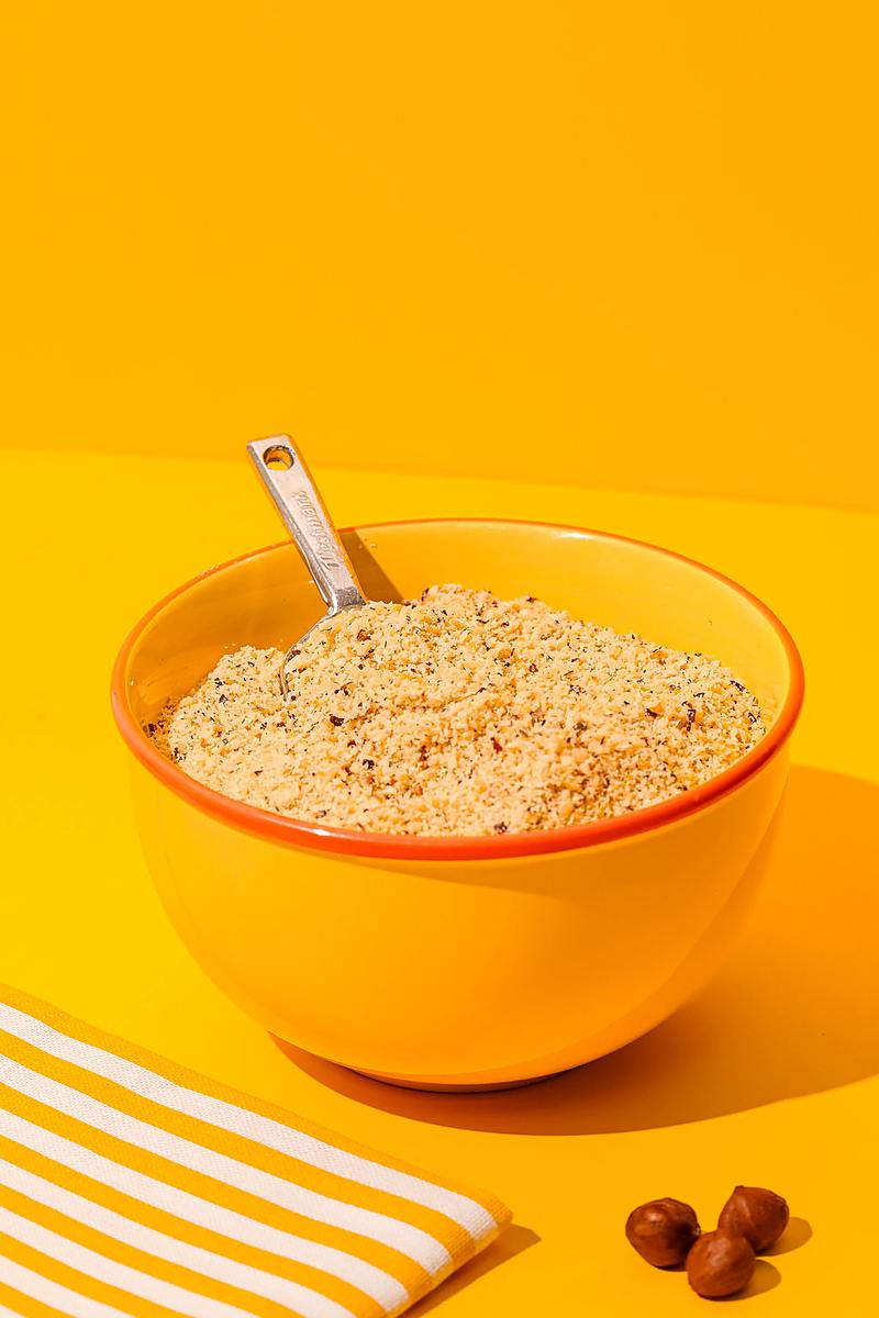 Poudre d'amandes dans un bol jaune avec une pelle en métal, sur fond jaune