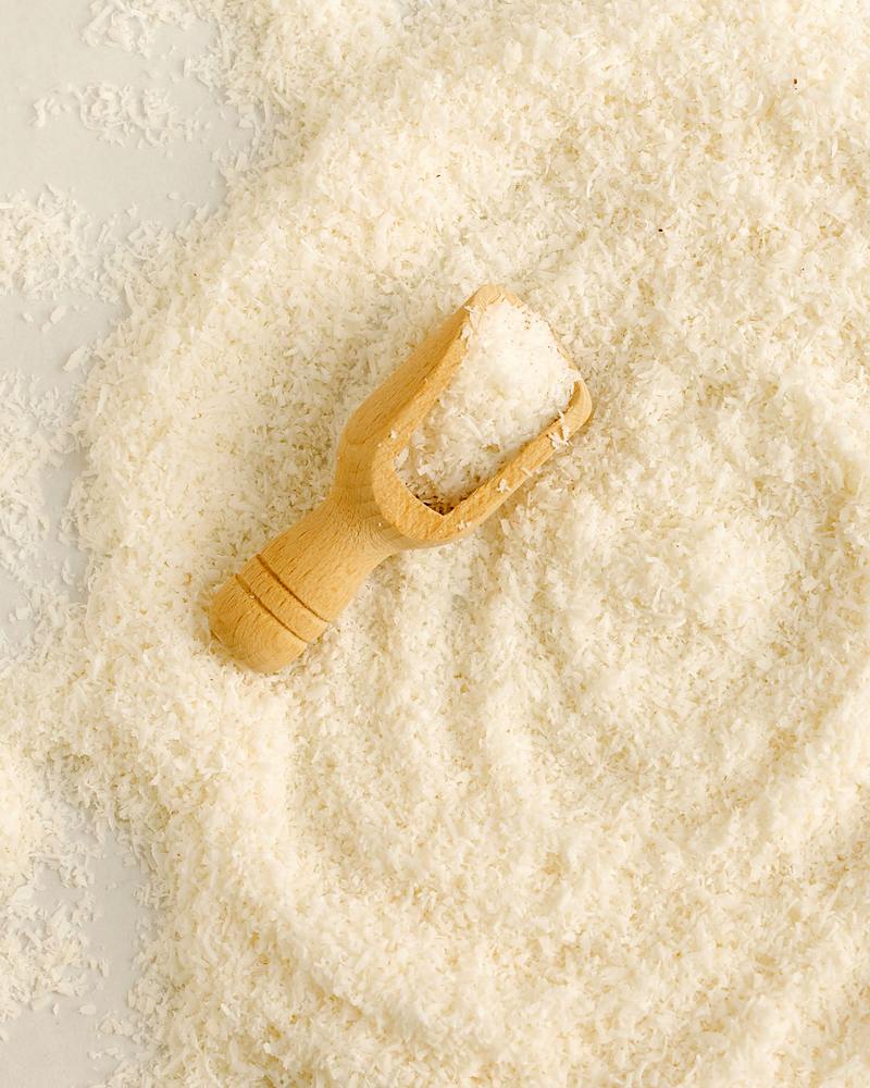 Coco râpé blanc en tas, avec une petite pelle en bois posée dessus