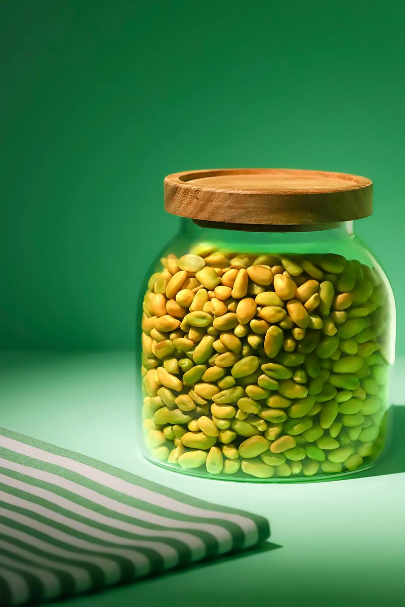 Pistaches émondées vertes dans un bocal en verre à couvercle en bois, sur fond vert
